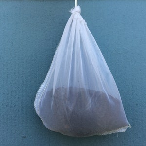 May include: A white mesh bag hanging from a string against a blue wall. The bag is filled with a dark substance.
