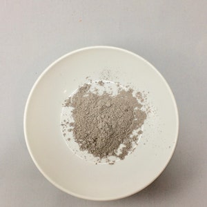 May include: A white ceramic bowl filled with a pile of gray powder.