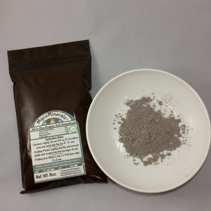 May include: A brown pouch with a white label that reads "MycoMinerals. All In One Organic Soil Amendment". The label lists application rates for gardens, existing plants, and potting soil. The pouch is sitting on a white surface next to a small white bowl filled with a gray powder.