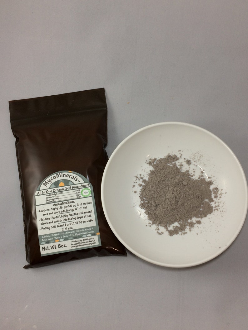 May include: A brown pouch with a white label that reads "MycoMinerals. All In One Organic Soil Amendment". The label lists application rates for gardens, existing plants, and potting soil. The pouch is sitting on a white surface next to a small white bowl filled with a gray powder.
