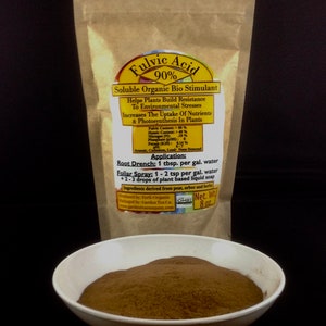 Może przedstawiać: Brązowa papierowa torba z etykietą, na kt&oacute;rej widnieje napis "Fulvic Acid 90% Soluble Organic Bio Stimulant". Etykieta zawiera listę składnik&oacute;w i instrukcje stosowania. Przed torbą stoi biała miska wypełniona brązowym proszkiem.