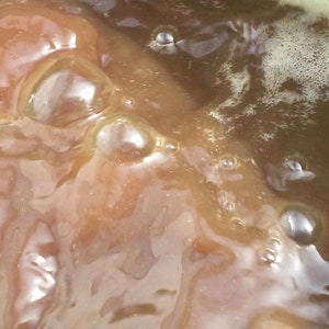 May include: Close-up of a brown liquid with bubbles forming on the surface. The liquid is in a clear container.