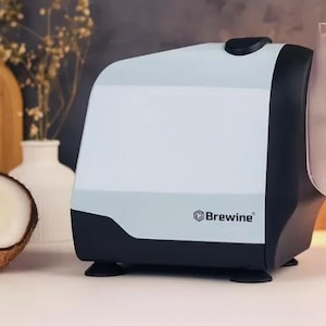May include: White and black electric coconut grater with a clear plastic cover and a stainless steel blade. The grater has the word "Brewine" printed on the front.