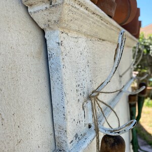 Peut inclure: &Eacute;tag&egrave;re murale en m&eacute;tal peint en blanc avec des crochets. L'&eacute;tag&egrave;re est orn&eacute;e d'une moulure d&eacute;corative sur le bord. Les crochets sont en m&eacute;tal et en forme de 'J'.