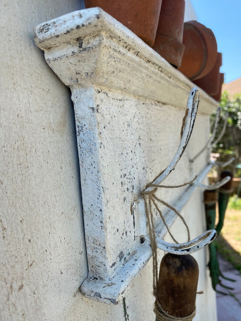 Peut inclure: &Eacute;tag&egrave;re murale en m&eacute;tal peint en blanc avec des crochets. L'&eacute;tag&egrave;re est orn&eacute;e d'une moulure d&eacute;corative sur le bord. Les crochets sont en m&eacute;tal et en forme de 'J'.