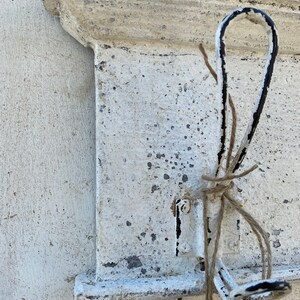 Peut inclure: &Eacute;tag&egrave;re en m&eacute;tal peinte en blanc avec un seul crochet en m&eacute;tal noir et blanc. Le crochet est entour&eacute; d'une ficelle brune.