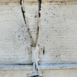Peut inclure: Un crochet en m&eacute;tal blanc avec des accents de peinture noire. Le crochet est fix&eacute; &agrave; une surface en bois blanc.