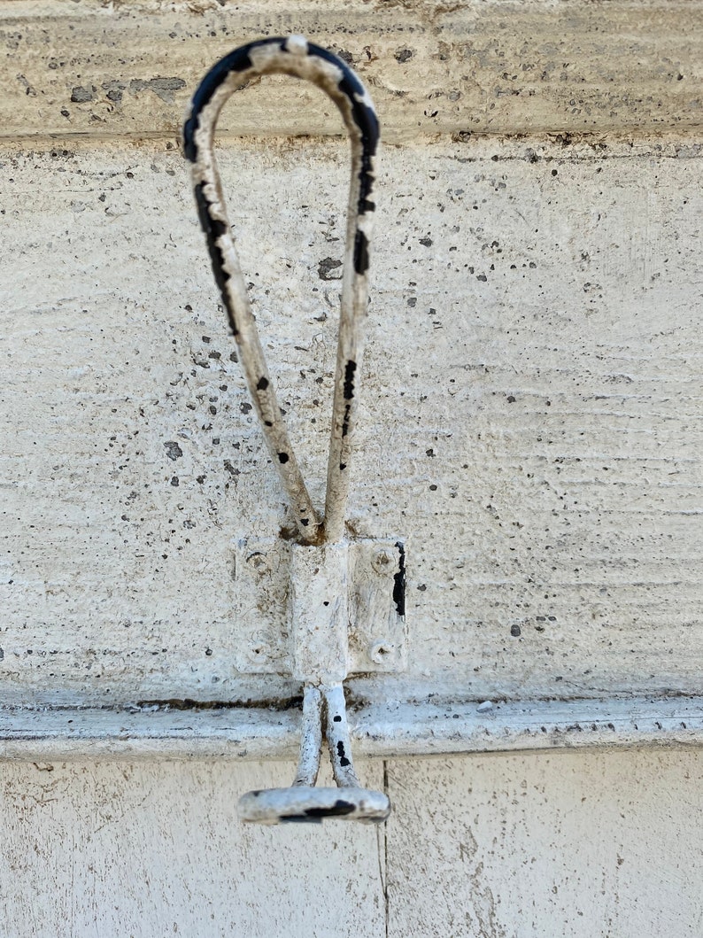 Peut inclure: Un crochet en m&eacute;tal blanc avec des accents de peinture noire. Le crochet est fix&eacute; &agrave; une surface en bois blanc.