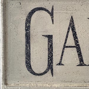 May include: White wooden sign with black lettering that reads "GARDEN". The sign has a distressed, vintage look.