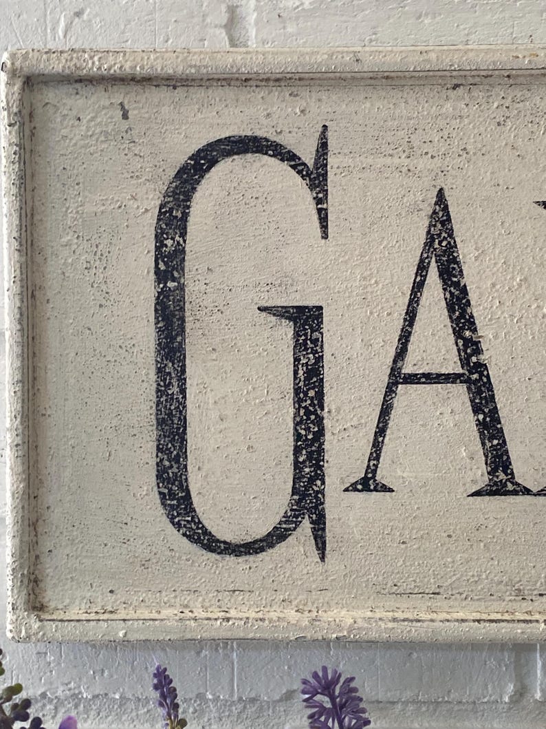 May include: White wooden sign with black lettering that reads "GARDEN". The sign has a distressed, vintage look.