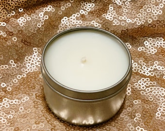 May include: A white candle in a silver tin container, sitting on a gold sequined fabric.
