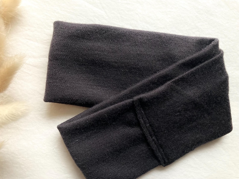 Puede incluir: Una diadema negra doblada de tela suave. La diadema es de color liso y parece estar hecha de un material el&aacute;stico. La diadema est&aacute; dise&ntilde;ada para usarse en la cabeza para mantener el cabello fuera de la cara.