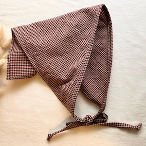 May include: A red and black checkered bonnet with a tie closure. The bonnet is made of a soft fabric and is designed to cover the head and neck. The checkered pattern is a classic design.