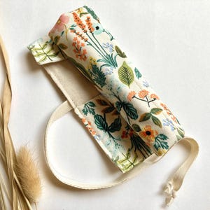 May include: A white canvas tote bag with a floral print featuring orange, green, and blue flowers. The bag has a single strap and a floral print lining.