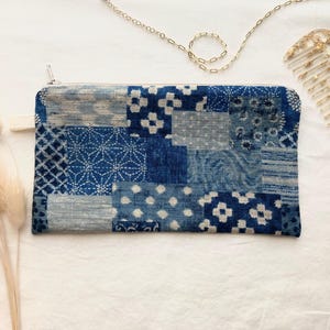 May include: A rectangular zippered pouch featuring a patchwork design of various blue and white fabric patterns. The textile displays geometric, floral, and abstract motifs in shades of indigo and light blue, finished with a silver-toned zipper.