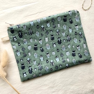 May include: A rectangular, sage green zipped pouch with a repeating pattern of stylized insects in navy, white, and light blue. The pouch has a white fabric pull tab and a silver zip.