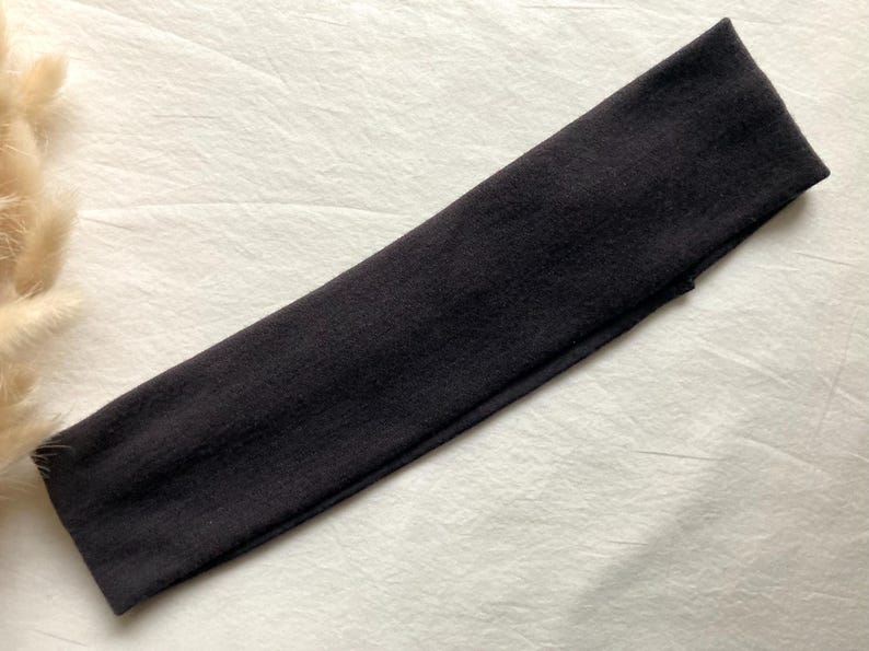 Puede incluir: Una diadema gris oscuro hecha de tela suave. La diadema es rectangular y parece el&aacute;stica. Est&aacute; sobre una superficie blanca y texturizada. La diadema es un accesorio para el cabello.