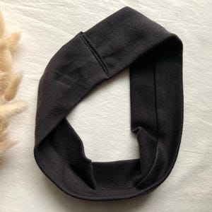Puede incluir: Una diadema negra de tela suave, dise&ntilde;ada como un bucle continuo. La diadema est&aacute; pensada para llevarla alrededor de la cabeza. El material parece ser de color liso, con un dise&ntilde;o sencillo y minimalista. La diadema es probablemente para moda o fitness.