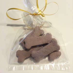 May include: A clear plastic bag tied with a gold ribbon, filled with several brown dog bone-shaped treats.