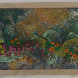May include: A framed artwork featuring a textured, abstract landscape with shades of green, brown, yellow, and white. The artwork is created with embroidery and fabric, giving it a unique and tactile quality.