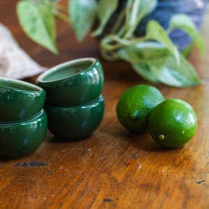 Puede incluir: Tres cuencos de cerámica verde apilados sobre una superficie de madera con dos limas verdes a su lado.