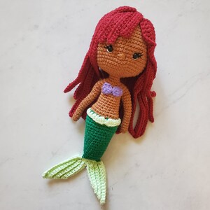 May include: Crocheted mermaid doll with red hair, brown skin, a purple top, and a green tail.