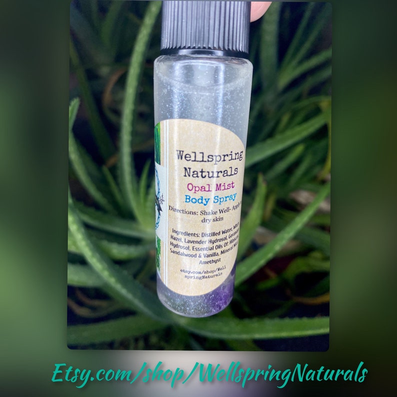 K&ouml;nnte beinhalten: Eine durchsichtige Glasflasche mit einer silbrig glitzernden Textur. Die Flasche ist mit "Wellspring Naturals Opal Mist Body Spray" beschriftet. Das Etikett enth&auml;lt auch Anweisungen zum Sch&uuml;tteln und Auftragen auf trockene Haut sowie eine Liste der Inhaltsstoffe. Die Flasche steht auf einer gr&uuml;nen Pflanze.