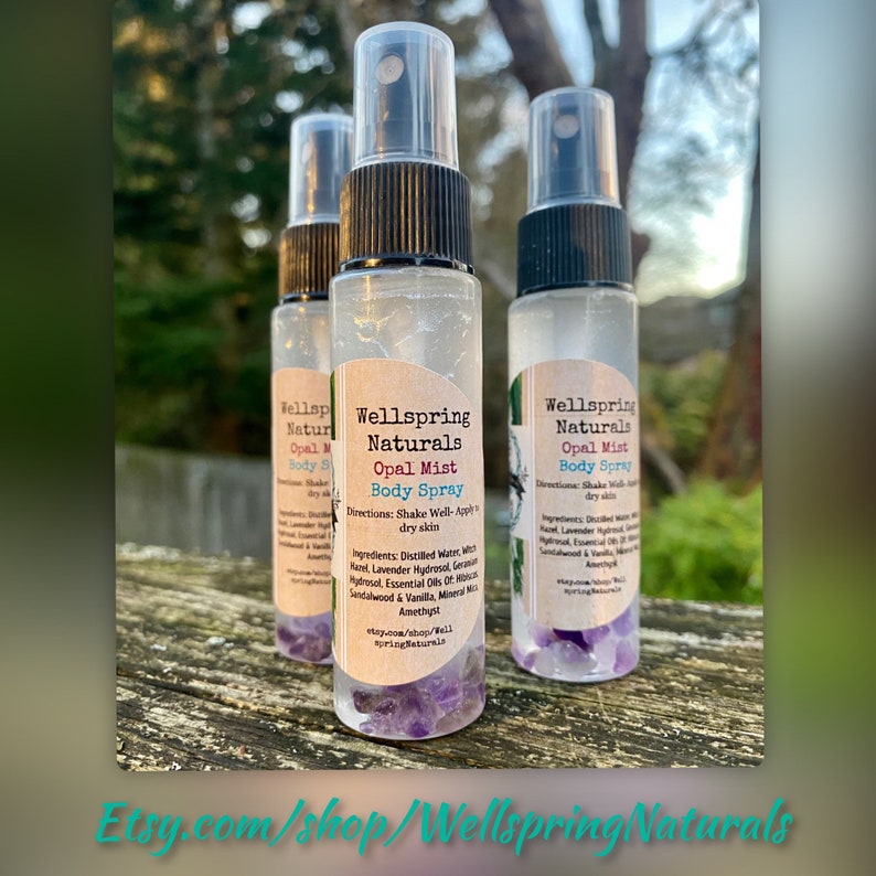 K&ouml;nnte beinhalten: Drei durchsichtige Glasflaschen mit schwarzen Spr&uuml;hk&ouml;pfen und Etiketten mit der Aufschrift "Wellspring Naturals Opal Mist Body Spray". Die Flaschen sind mit einer klaren Fl&uuml;ssigkeit gef&uuml;llt und enthalten am Boden kleine lila Kristalle. Die Etiketten enthalten auch Gebrauchsanweisungen und eine Zutatenliste.