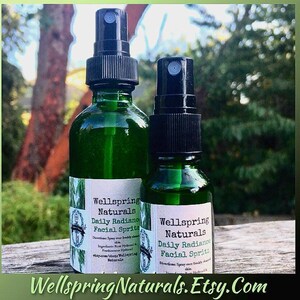 Puede incluir: Dos botellas de spray de vidrio verde de Wellspring Naturals Daily Radiance Facial Spritz. Las botellas tienen boquillas de spray negras y etiquetas blancas con información del producto. El nombre de la tienda Etsy está en la parte inferior.