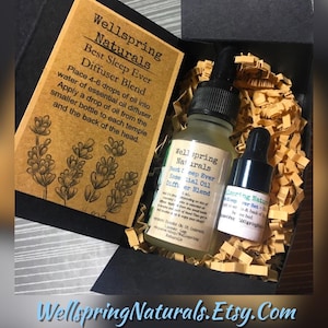 May include: A black gift box containing two glass bottles with black dropper caps and a tan instruction card. The card features the text Wellspring Naturals Best Sleep Ever Diffuser Blend and lavender illustrations. The bottles have matching labels.