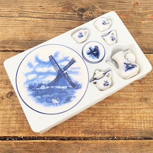 Può includere: Un servizio da tè in miniatura in porcellana con un motivo a mulino a vento blu e bianco. Il set include un piatto, tazze, piattini, una teiera e una lattiera, il tutto in un vassoio bianco. Il motivo del mulino è ripetuto.
