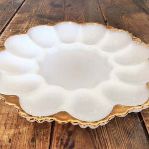 May include: White, scalloped egg serving dish with a gold rim. The dish has a central area surrounded by 12 individual egg cup sections. The gold rim adds a touch of elegance to this vintage-style serving piece.