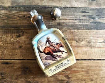 1970年代ヴィンテージのジムビームズチョイスケンタッキーストレートバーボンウイスキーデカンタ。フレデリック・レミントンのアートワーク「カウボーイ」が描かれている。バーの装飾品。
