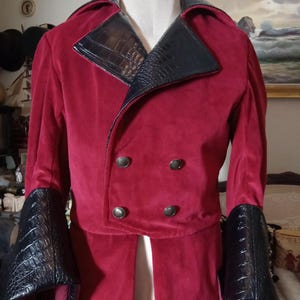May include: A double-breasted red jacket featuring a wide collar and cuffs made of black faux leather with a crocodile-skin texture. The jacket has four round metallic buttons arranged in two rows on the front and a long, structured silhouette.