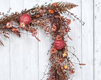 May include: A long, cascading floral garland with pink and orange flowers and dried foliage. The garland is hanging on a white wooden door.