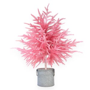 May include: A pink artificial Christmas tree in a galvanized metal bucket. The tree has a full, textured appearance with many small, feathery branches. The bucket has a handle on each side and a speckled finish. The tree is a decorative item.