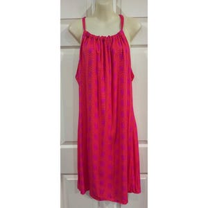 May include: A sleeveless, knee-length dress in a vibrant pink hue, adorned with a repeating orange wave pattern. The dress features thin straps and a gathered neckline, displayed on a mannequin.