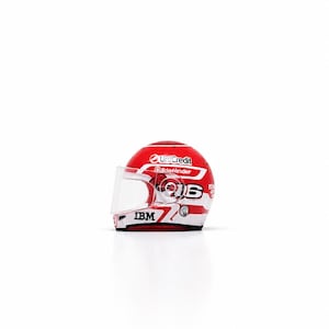 May include: A miniature red and white racing helmet featuring a clear visor, the number 16, and corporate logos including UniCredit, Bitdefender, and IBM printed on the exterior surface. The helmet has a glossy finish and a streamlined design.