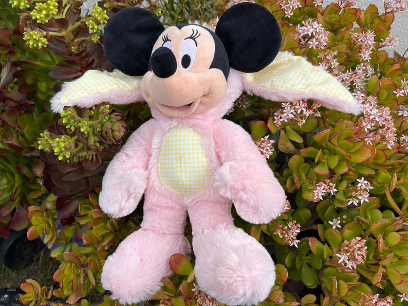 May include: Pink plush Mickey Mouse dressed in a yellow and white gingham bunny costume with long floppy ears.