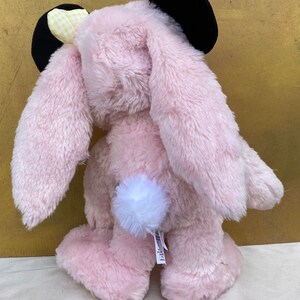 May include: Pink plush bunny rabbit toy with black ears and a yellow and white checkered bow. The bunny has a white fluffy tail.