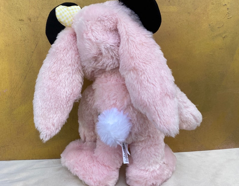 May include: Pink plush bunny rabbit toy with black ears and a yellow and white checkered bow. The bunny has a white fluffy tail.