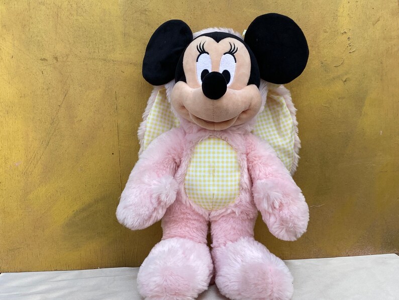 May include: Pink plush Easter bunny with yellow and white gingham fabric on the chest and ears. The bunny has black ears and a black nose. The bunny is a Mickey Mouse character.