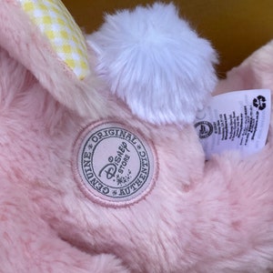 May include: Pink plush bunny with a white pom-pom tail and a yellow and white checkered bow. The bunny has a tag that says "Genuine Original Disney Store Authentic".