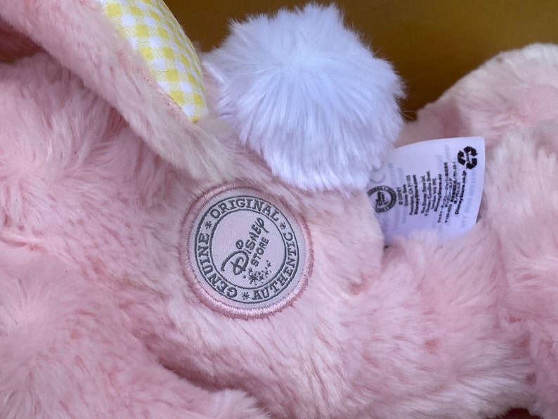 May include: Pink plush bunny with a white pom-pom tail and a yellow and white checkered bow. The bunny has a tag that says "Genuine Original Disney Store Authentic".