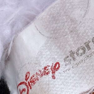 K&ouml;nnte beinhalten: Wei&szlig;er Stoff mit einem roten Disney-Logo und einem grauen "akros"-Logo mit dem Text "www.akrosdesign.com".