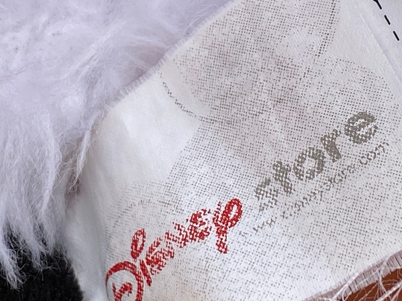 K&ouml;nnte beinhalten: Wei&szlig;er Stoff mit einem roten Disney-Logo und einem grauen "akros"-Logo mit dem Text "www.akrosdesign.com".