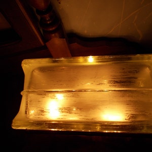 Peut inclure: Un bloc de verre transparent avec deux lumi&egrave;res chaudes qui brillent &agrave; travers. Le bloc est rectangulaire et a une surface lisse.