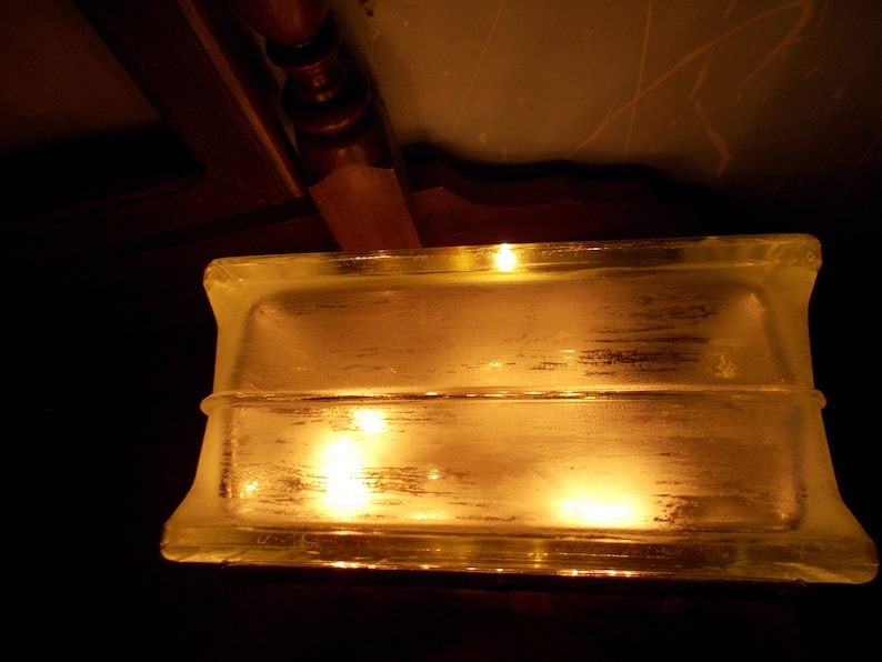 Peut inclure: Un bloc de verre transparent avec deux lumi&egrave;res chaudes qui brillent &agrave; travers. Le bloc est rectangulaire et a une surface lisse.