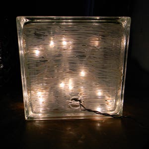 Peut inclure: Un bloc de verre transparent avec une surface textur&eacute;e et plusieurs petites lumi&egrave;res &agrave; l'int&eacute;rieur. Les lumi&egrave;res illuminent le bloc de verre de l'int&eacute;rieur, cr&eacute;ant une lueur chaleureuse.