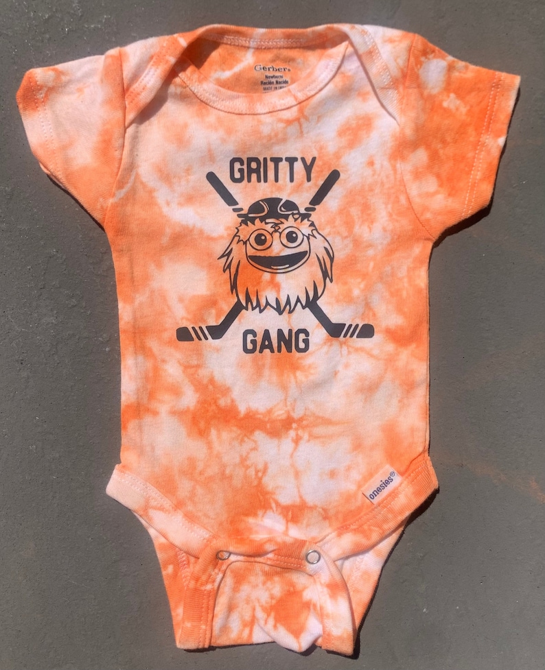 May include: Orange and white tie-dye baby onesie with a black graphic of Gritty, the Philadelphia Flyers mascot, with the text "Gritty Gang".